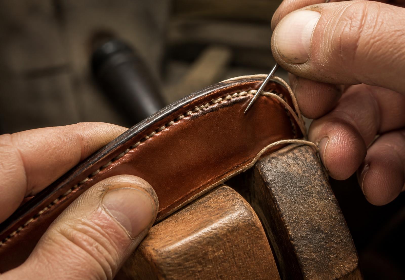 Artisan hand stitching the edge of a leather belt